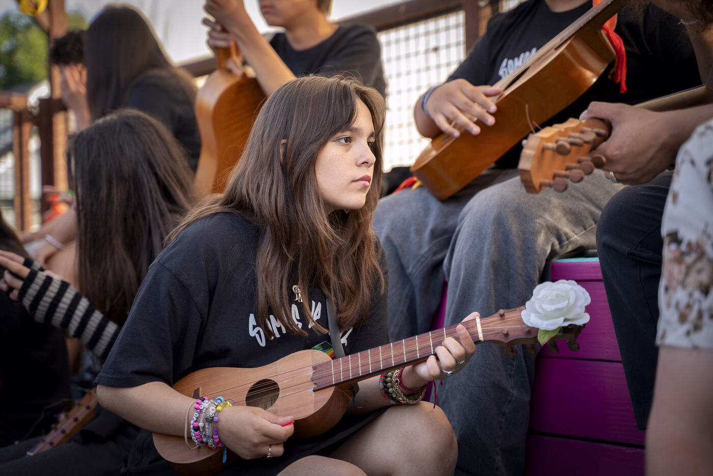 Young people play ukuleles and guitars together at an outdoor event.
