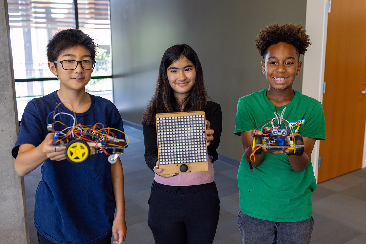 Three students proudly hold up the electronics projects they built.