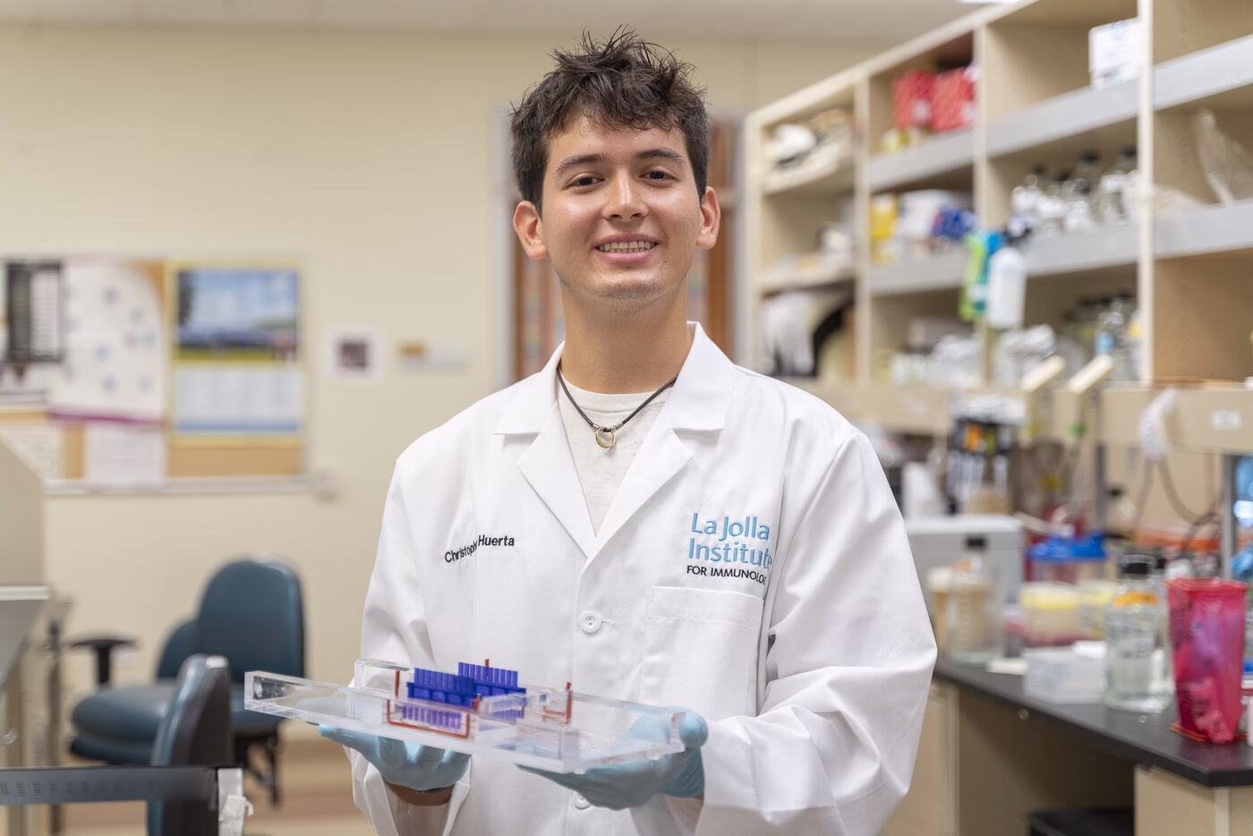 A teenager in a white lab coat holds sample tubes in a research laboratory.