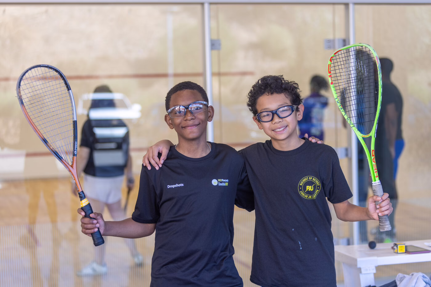 Two young people hold rackets on an indoor squash court.