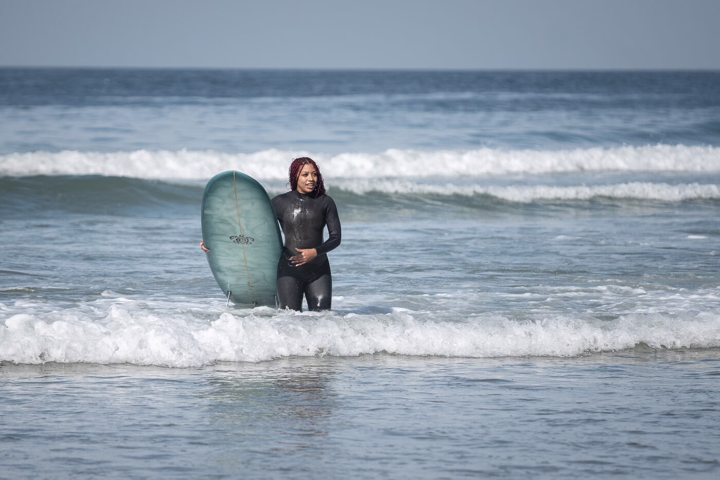 A young woman carries her surfboard out of the ocean.